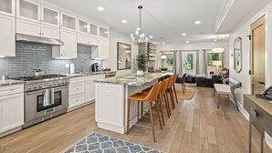 A modern kitchen with white cabinets, a central island, and a dining area with bar stools.