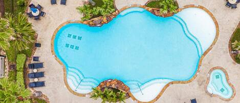 An aerial view of a swimming pool with surrounding lounge areas, palm trees, and a stone border.