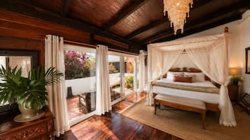 Un dormitorio con cama a dosel, suelo de madera, un ventanal con cortinas y una planta en maceta.