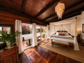 Un dormitorio con cama a dosel, suelo de madera, un ventanal con cortinas y una planta en maceta.