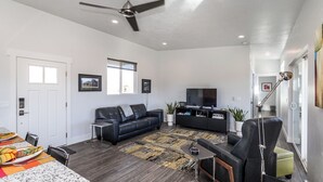 A modern living room with a black leather sofa, a TV, and a ceiling fan. - Exceptional Vacation Home - 1 bdr in Torrey, UT near Capital Reef National Park (Torrey)