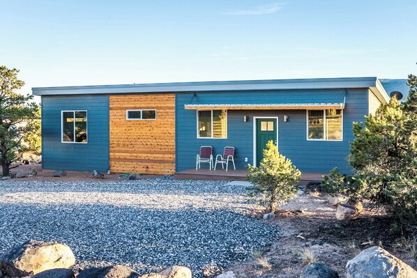A modern two-story house with a blue exterior, a wooden front door, and a small porch with two chairs. - Exceptional Vacation Home - 1 bdr in Torrey, UT near Capital Reef National Park (Torrey)