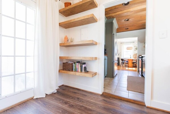A hallway with wooden shelves, a door, and a view into a dining area.