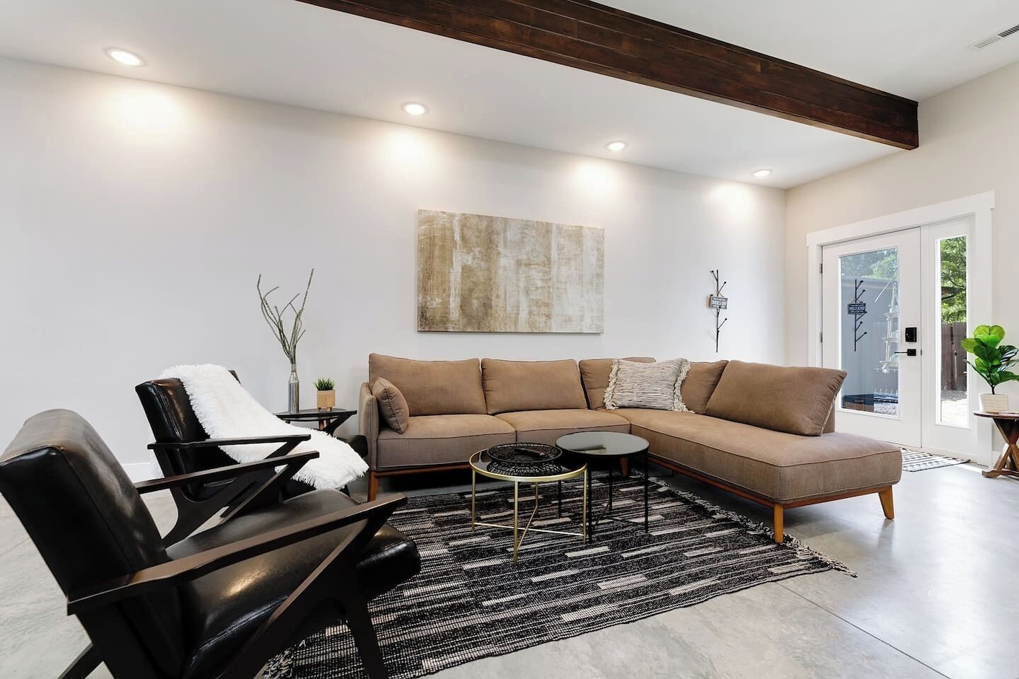 A modern living room with a sectional sofa, a black leather chair, a round coffee table, and a black and white rug.