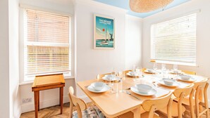 A dining room with a wooden table set for six, white chairs, and a poster of The Broads National Park on the wall. - Gorleston Beach House by Leap Escapes (Gorleston-on-Sea)
