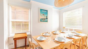 Une salle à manger avec une table en bois dressée pour six personnes, des chaises blanches et une affiche du parc national de The Broads accrochée au mur.