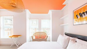 A bedroom with a bed, a wicker chair, a window, and a wall art piece. - Gorleston Beach House by Leap Escapes (Gorleston-on-Sea)