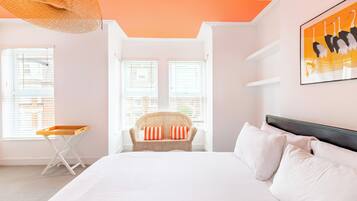 Une chambre à coucher avec un lit, une chaise en osier, une fenêtre et une œuvre d’art murale.