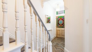 A staircase with white balusters leading to a landing, a herringbone-patterned floor, and a wooden door with a colorful geometric window. - Gorleston Beach House by Leap Escapes (Gorleston-on-Sea)