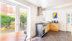 A modern kitchen with a gas stove, oven, and a large window overlooking a garden. - Gorleston Beach House by Leap Escapes (Gorleston-on-Sea)
