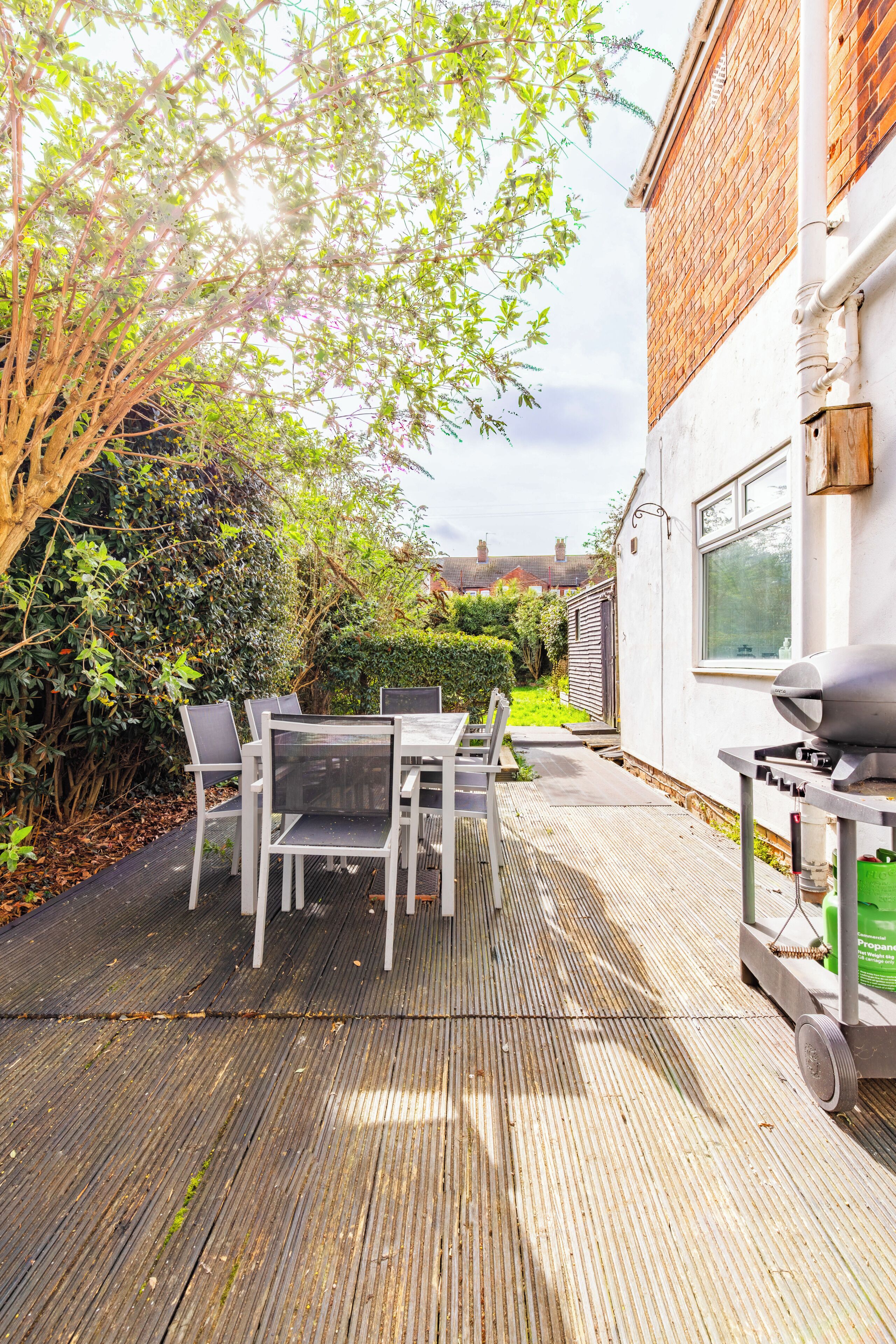 A patio with a table and chairs, a grill, and a white building in the background.