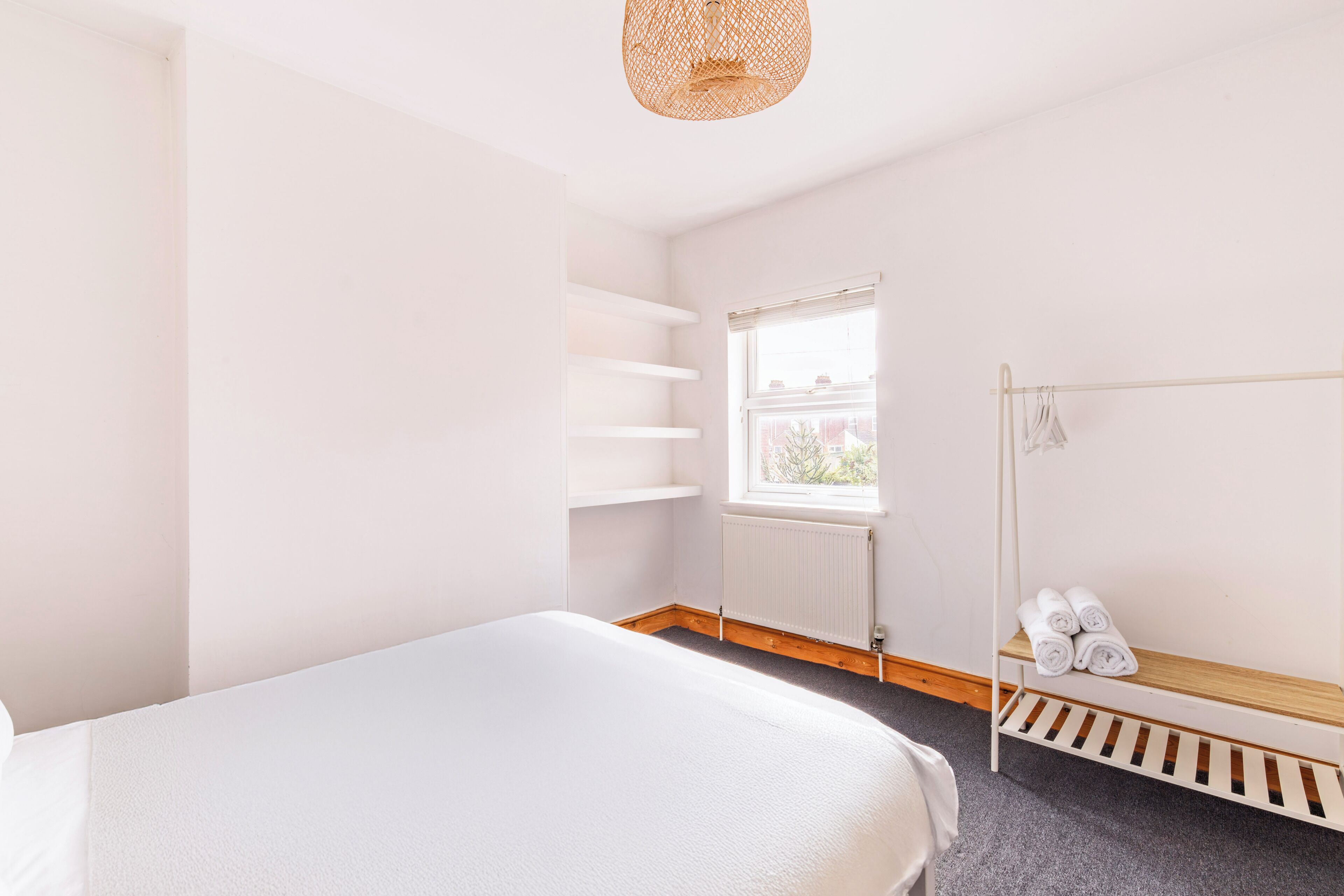 A bedroom with a bed, a window, a radiator, and a shelf with towels.