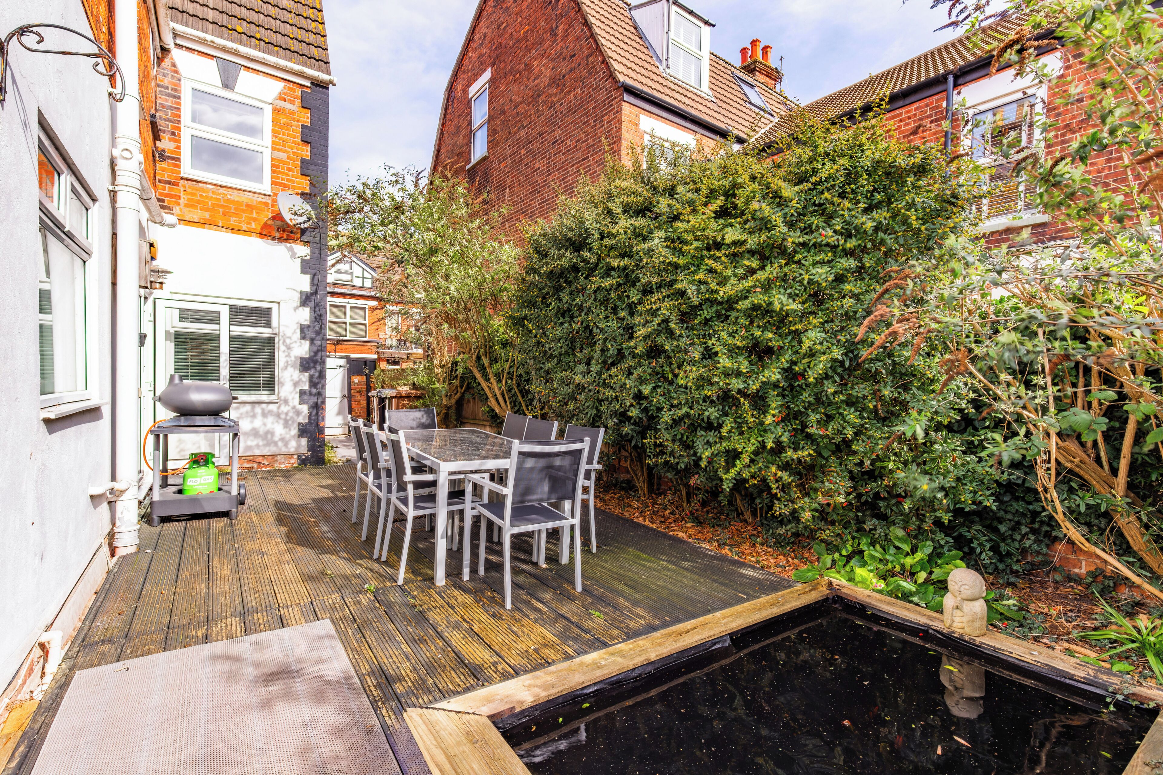 A courtyard with a wooden deck, a table with chairs, and a small pond.