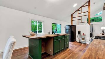 Une cuisine dotée d’un plan de travail en bois, de meubles de rangement verts, d’une cuisinière encastrée et offrant une vue sur la verdure par les fenêtres.