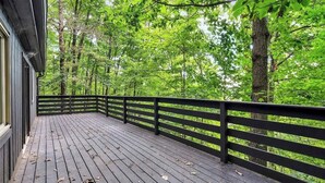 A wooden deck with a black railing, surrounded by lush green trees.