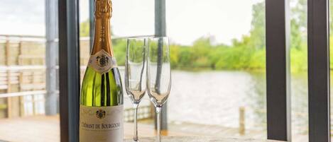 Una botella de champán Cuvée de Bourgogne y dos copas de champán vacías sobre una mesa con vista a un río y vegetación.