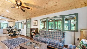 A spacious living room with a plaid sofa, a coffee table, and a dining area with chairs and a table. - Lakefront Cabin on Watts Bar Lake | Private Dock & Views (Roane County)