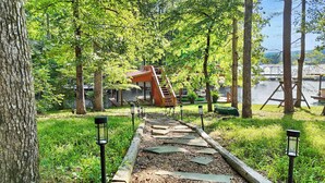 A wooden pathway leading to a wooden structure with a staircase, surrounded by trees and a body of water. - Lakefront Cabin on Watts Bar Lake | Private Dock & Views (Roane County)