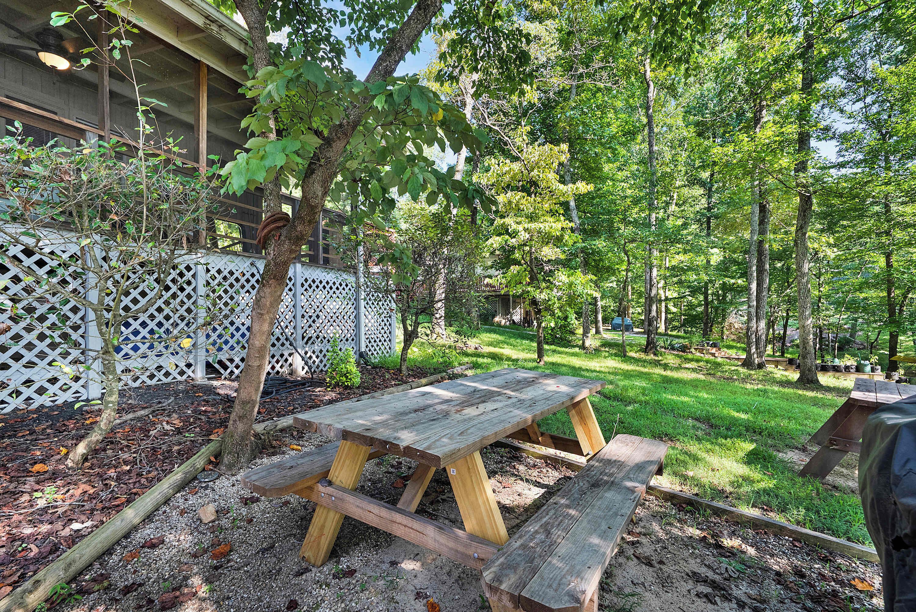 A wooden picnic table in a garden with a white lattice fence and trees.