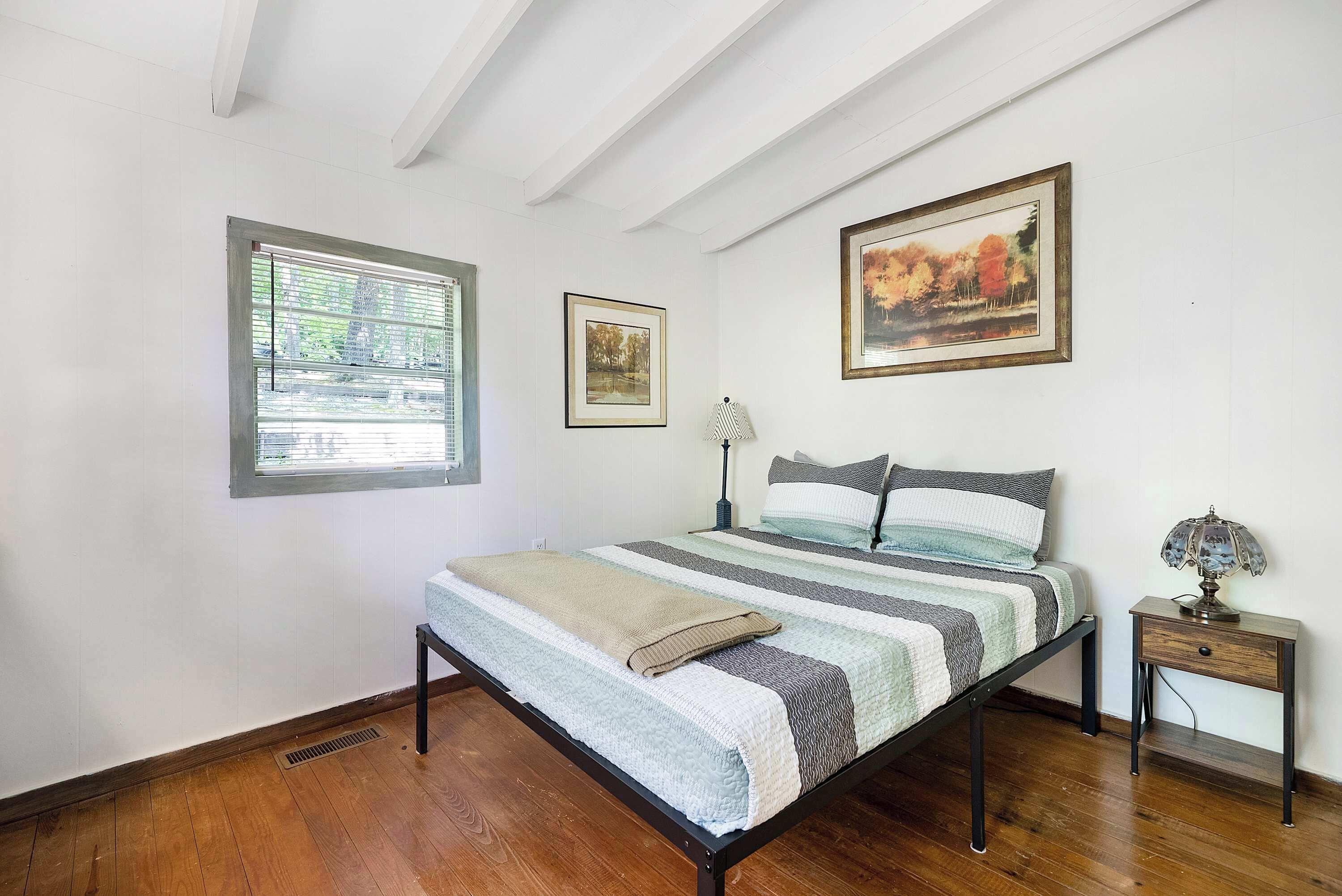 A bedroom with a bed, a nightstand, a lamp, and two framed pictures on the wall.