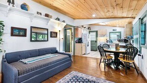 A cozy living room with a sofa, dining table, and chairs. There is a kitchen area with cabinets and appliances visible in the background. - Lakefront Cabin on Watts Bar Lake | Private Dock & Views (Roane County)