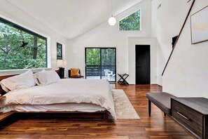 Un dormitorio moderno con una cama grande, un banco y vistas al exterior a través de una puerta corredera.