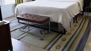 Een slaapkamer met een bed, een bankje, een raam en een plafondventilator.