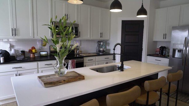 Een moderne keuken met witte kasten, een groot eiland met barkrukken, een zwarte kraan en hanglampen.
