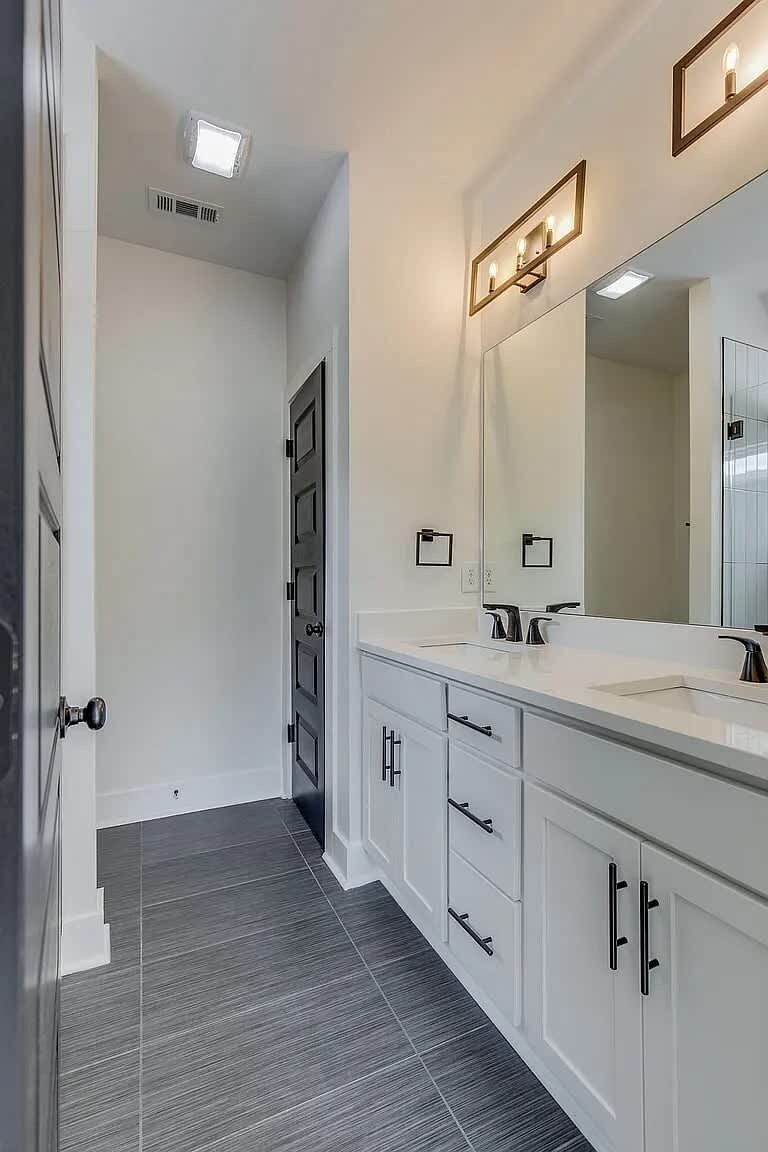 A modern bathroom with a large mirror, two sinks, and a walk-in shower.