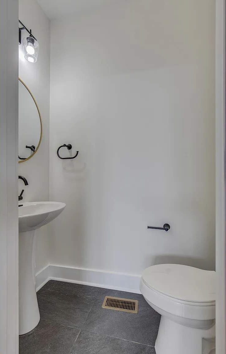 Une salle de bain avec un lavabo, des toilettes et une douche, le tout de couleur blanche. Un luminaire est installé au-dessus du lavabo et un porte-serviettes est fixé au mur.