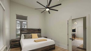 Une chambre à coucher avec un grand lit, un ventilateur de plafond, une fenêtre et une porte donnant sur une autre pièce.