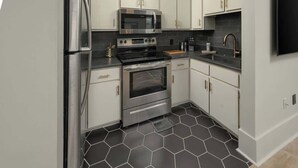 Une cuisine moderne dotée d’appareils électroménagers en acier inoxydable, de meubles blancs et d’un sol carrelé de motifs hexagonaux noirs.