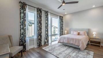 A bedroom with a bed, a chair, a ceiling fan, and a window with curtains.
