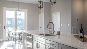 Una cocina moderna con una isla grande, pileta de acero inoxidable e iluminación colgante.