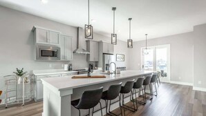Una cocina moderna con una isla central, taburetes de bar, electrodomésticos de acero inoxidable e iluminación colgante.