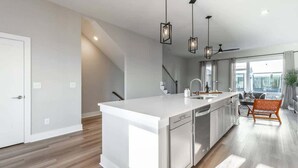 Una cocina moderna con una isla blanca, electrodomésticos de acero inoxidable, iluminación colgante y vistas al área de estar.