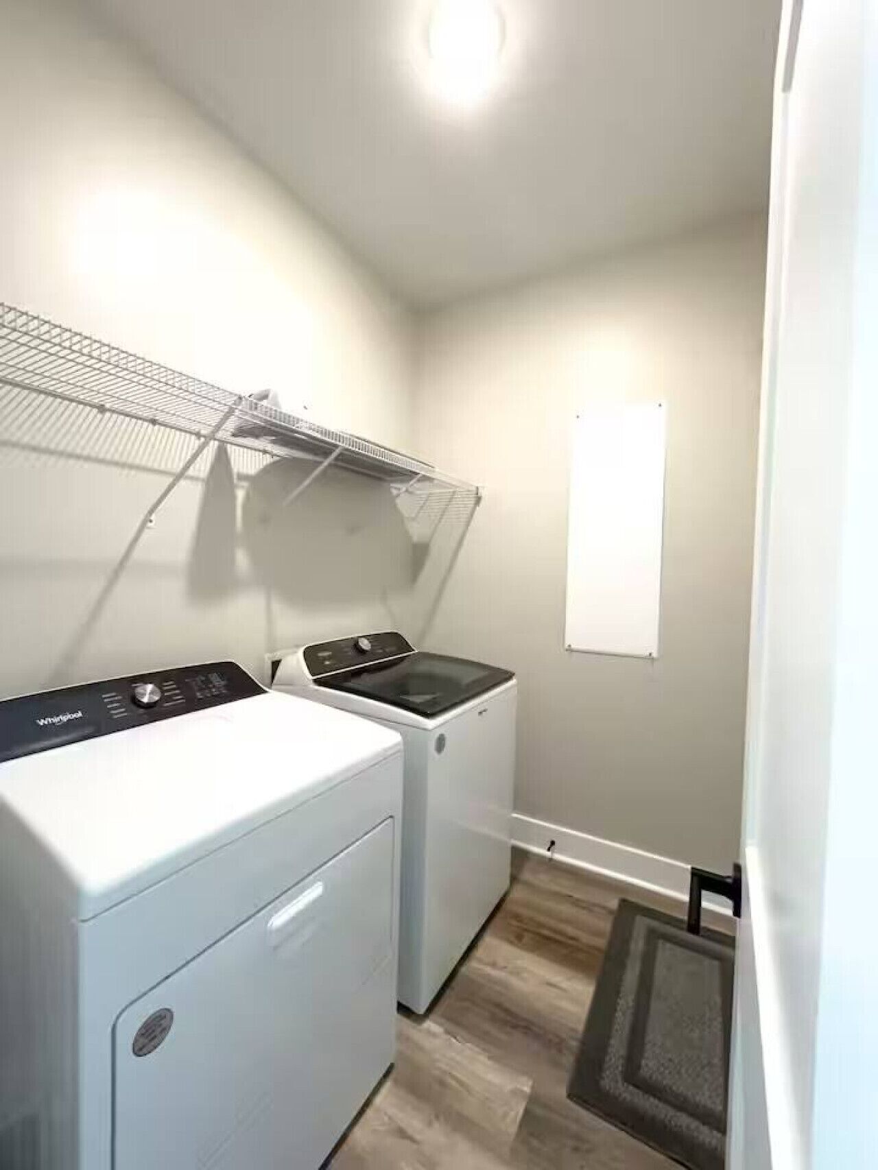 Une buanderie équipée d’un lave-linge et d’un sèche-linge à chargement frontal, d’un étendoir métallique et d’un tableau blanc fixé au mur.