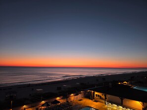 Une vue sur la plage au coucher du soleil, avec une piscine et un bâtiment doté d’une terrasse.