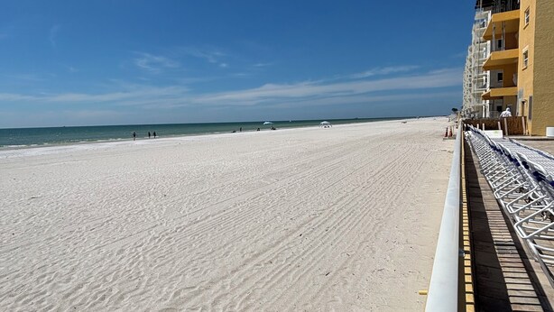 Een strand met een heldere lucht, een zandstrand en een gebouw met meerdere balkons.