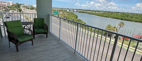 A balcony with two wicker chairs, a view of a river, and a bridge in the distance.