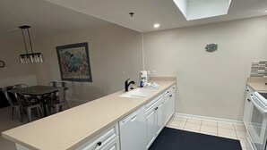 Een moderne keuken met dakraam, witte kasten, een zwart kleed en een eethoek met stoelen en een tafel.