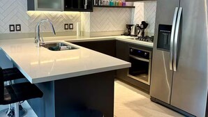 A modern kitchen with a central island, stainless steel appliances, and a herringbone-patterned backsplash. - Versalles Corner (Puerto Vallarta)