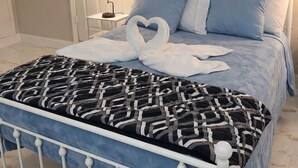 Siististi pedattu sänky, jossa on kuviollinen peitto, sydämenmuotoinen pyyheasetelma ja yöpöydällä oleva lamppu.