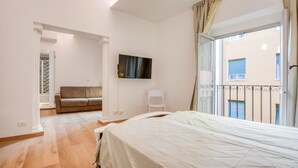 Quarto com cama, televisão na parede, varanda com guarda-corpo e vista para o edifício exterior.