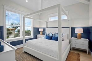 A four-poster bed with white bedding, two bedside tables with lamps, and a view of the outdoors through large windows. - Brand New beach house! Heated pool and spa! (Bradenton Beach)