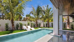 Una piscina con lettini, circondata da palme e da un recinto bianco.