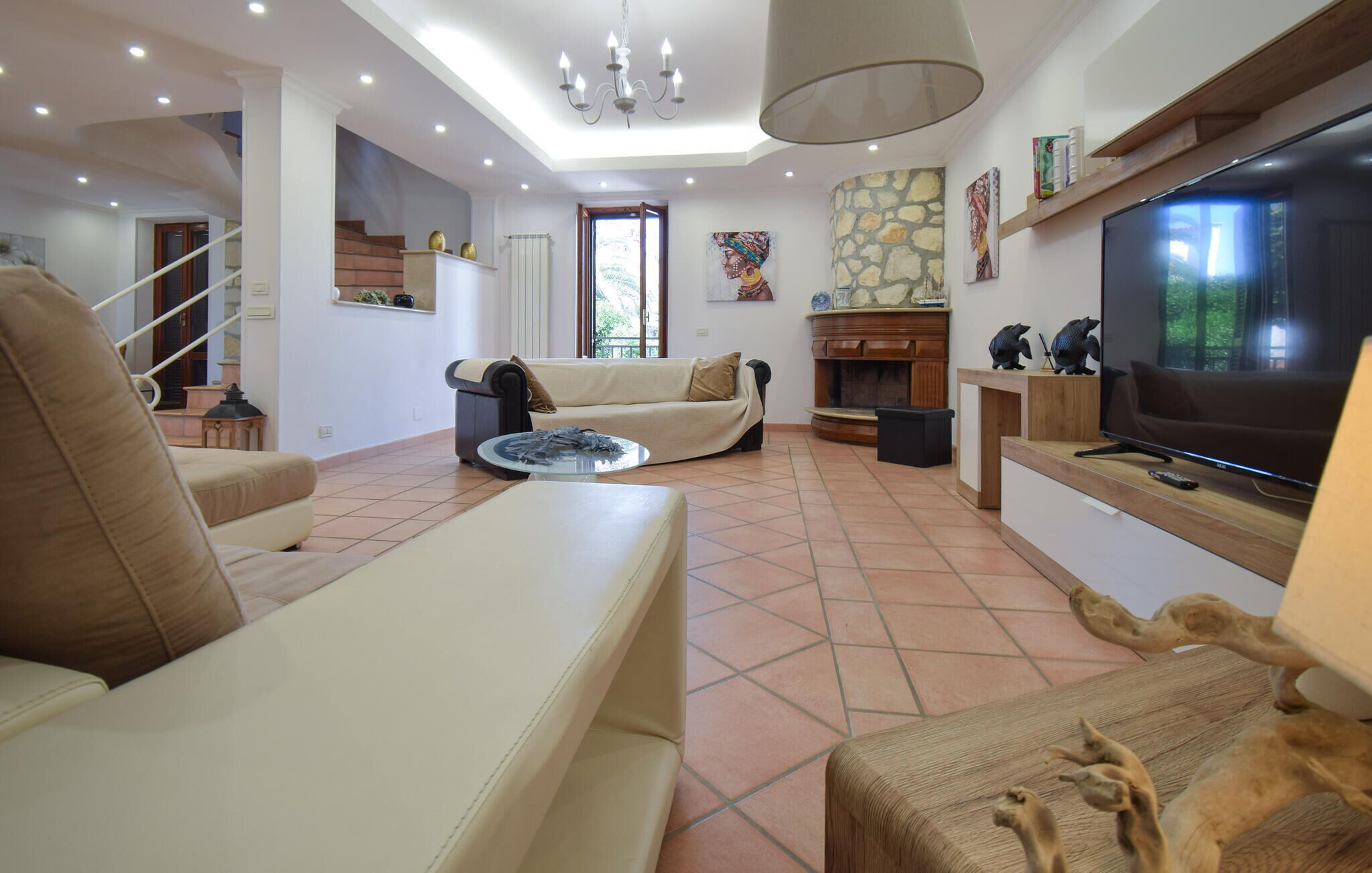 A spacious living room with a large TV, comfortable seating, a fireplace, and a staircase leading to an upper level.