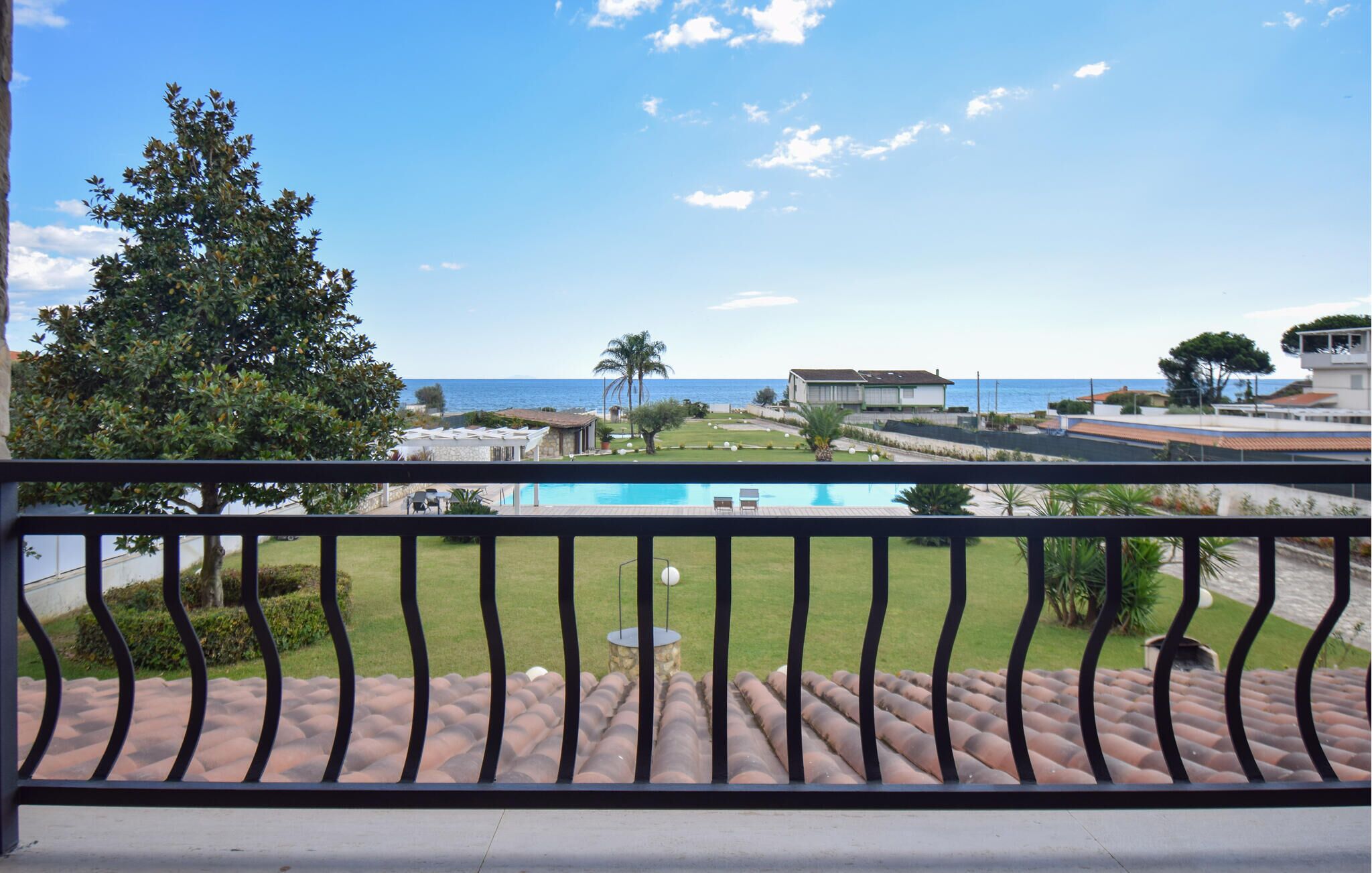 A balcony with a view of a swimming pool, a lawn, and a beach.