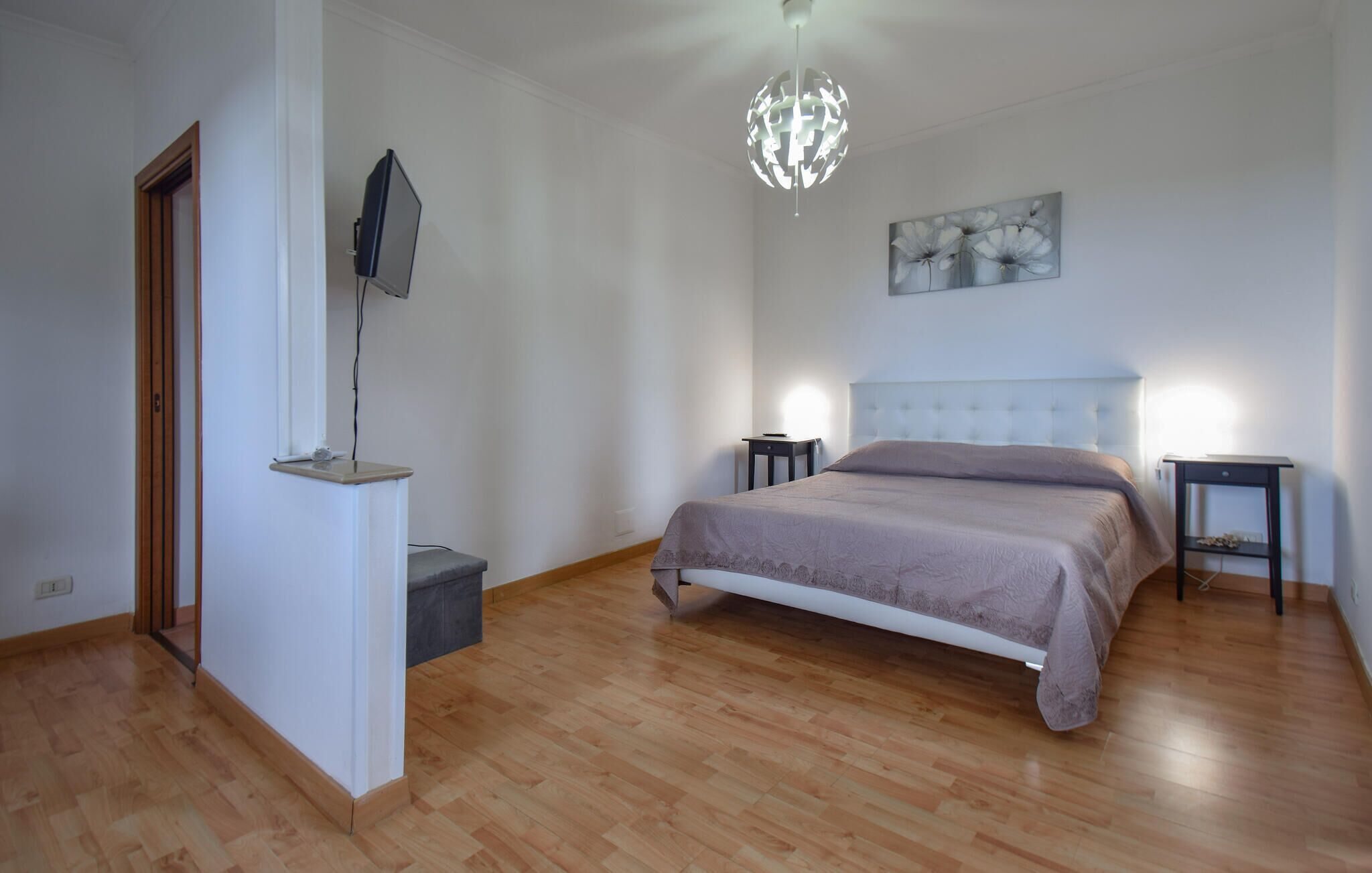 A bedroom with a bed, a bedside table, a nightstand, a hanging light fixture, and a painting on the wall.