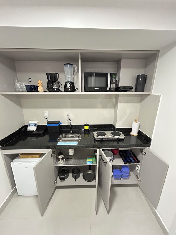 A compact kitchen with a black countertop, a coffee maker, a microwave, and a sink. - Melhores Flats - Delícia a 50m do mar (João Pessoa)
